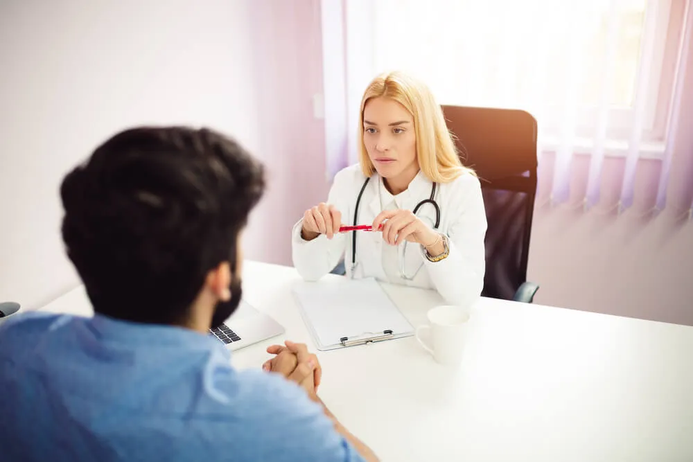 Médica conversa com paciente durante avaliação clínica em consulta relacionada a exame demissional