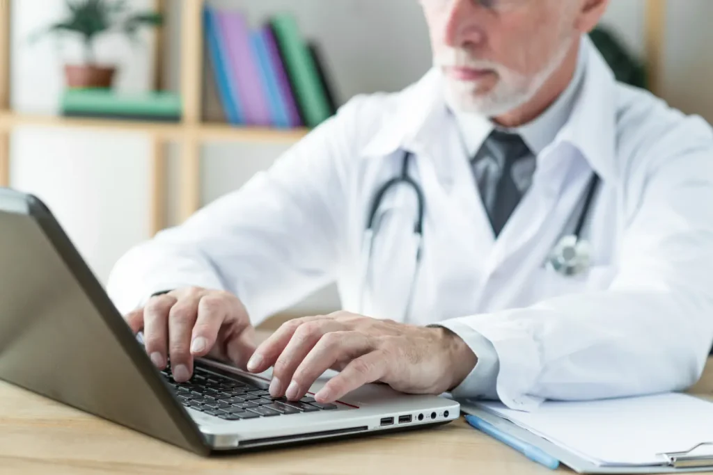 Medico elaborando laudo medico em computador com estetoscópio sobre a mesa